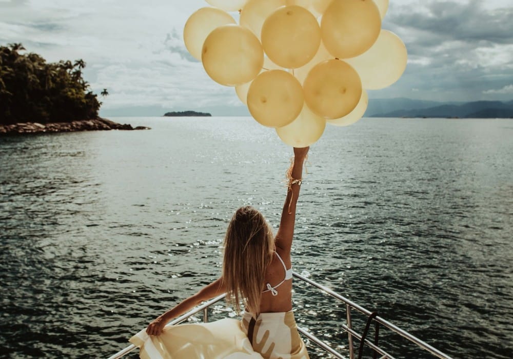 Woman in yellow dress with yellow balloons on front of boat