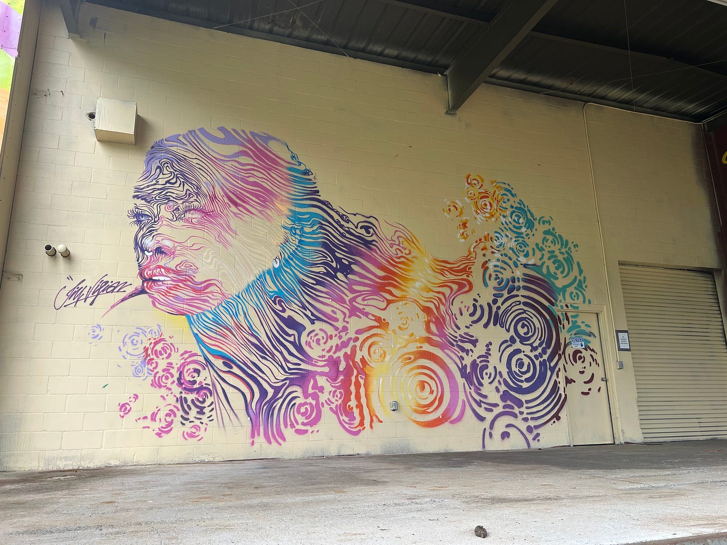 Street mural from Kauai of a woman's face and long hair painted in rainbow colored swirls