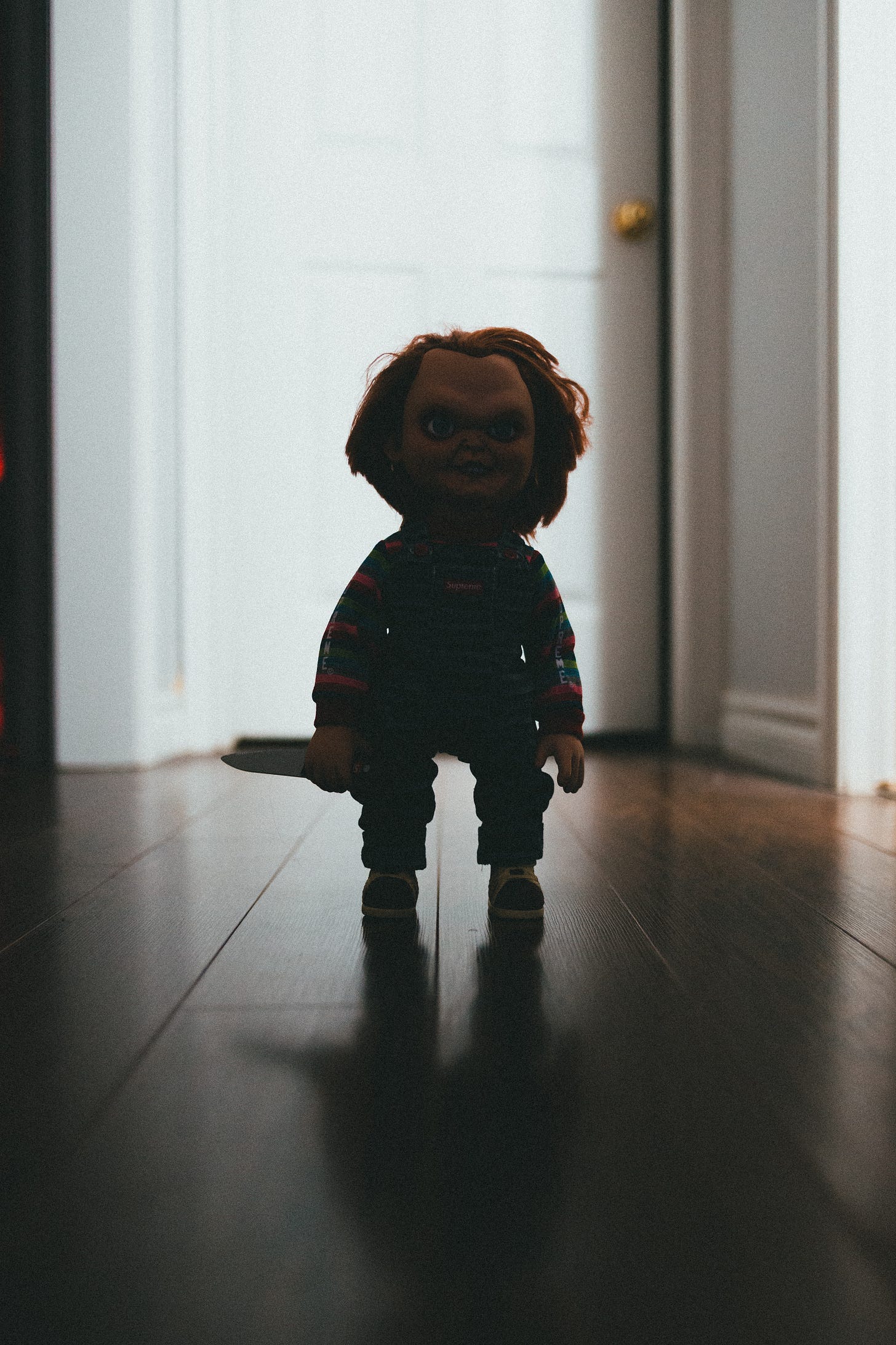 A photograph of Chucky the killer doll standing in a hallways wielding a knife.