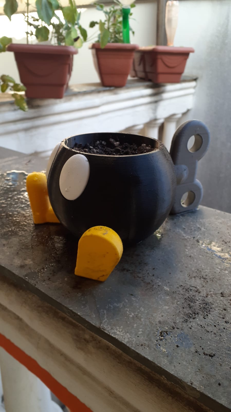 Um vaso na forma do personagem Bom-omb: uma bomba preta com olhos brancos, sapatos amarelos e uma chave de dar corda às costas.