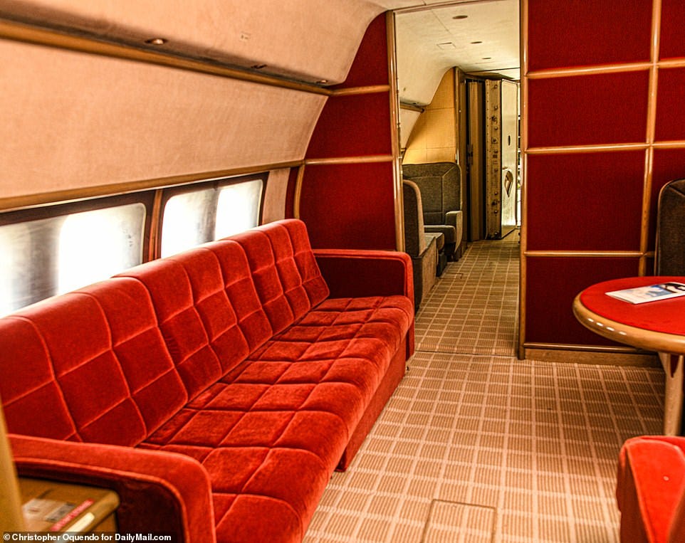 The private plane's red garish couch sits in the middle of the plane with an executive table and chairs