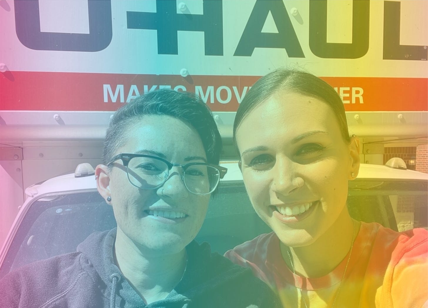 A rainbow-filtered photograph of Shohreh and her partner Jessie smiling and sitting together on the hood of a U-Haul truck