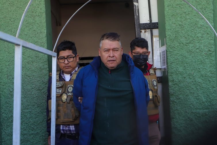 A man being led out of a prison cell by Bolivian police officers.