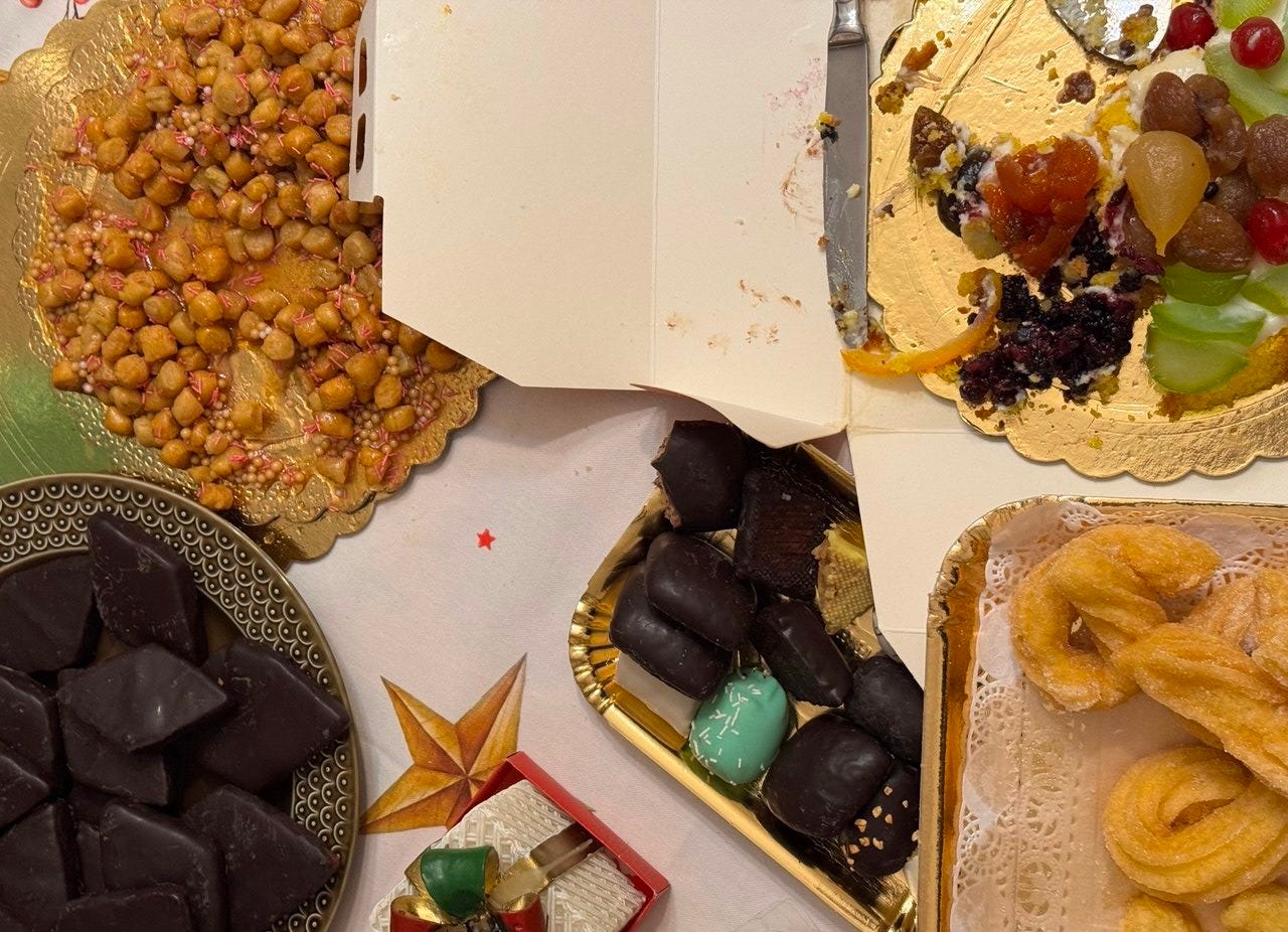 L'immagine rappresenta tanti tipi di dolci natalizi su un tavolo. Da sinistra: gli struffoli, una cassata siciliana, mustaccioli e zeppole natalizie
