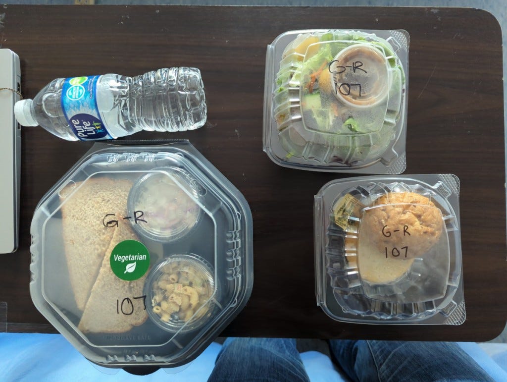 Sample lunch: a sandwich, salad, and roll in plastic packaging, plus a bottle of water.