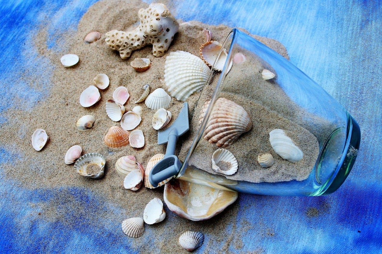 Shells and sand spilling out of a glass jar