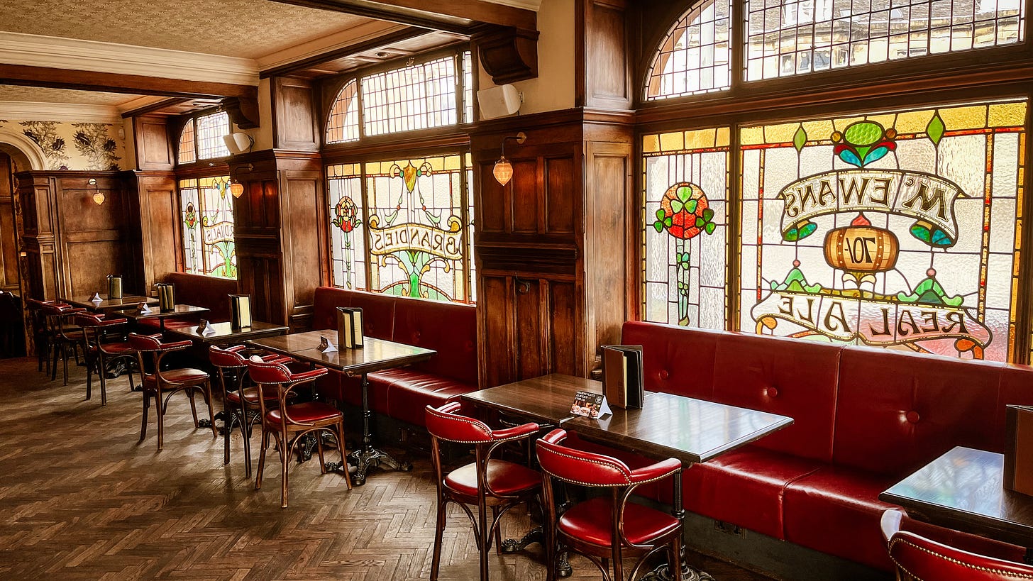 Sun shines through stained glass windows in the interior of Ryrie's, which has wooden parquet flooring and red leather seating.