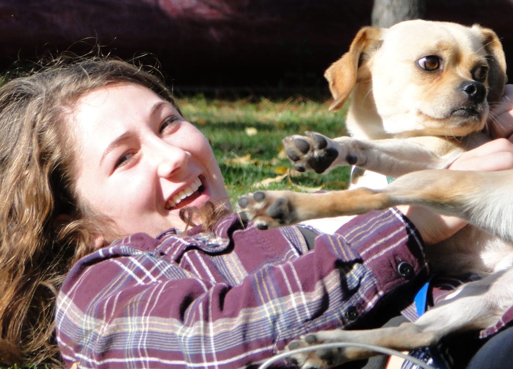 A teenage girl wrestles playfully with a small dog on the grass