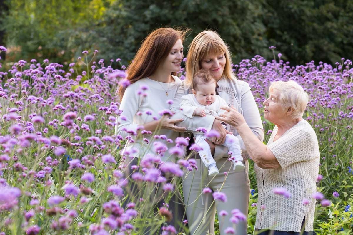 Great-grandmother, grandmother, mother holding a baby outdoors.