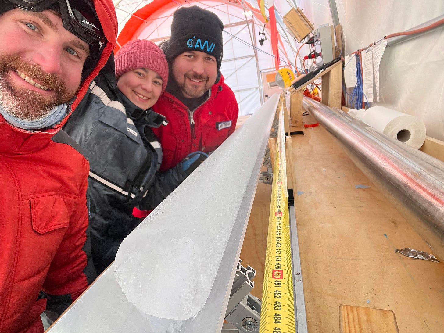 Three smiling researchers bundled up over an ice core.