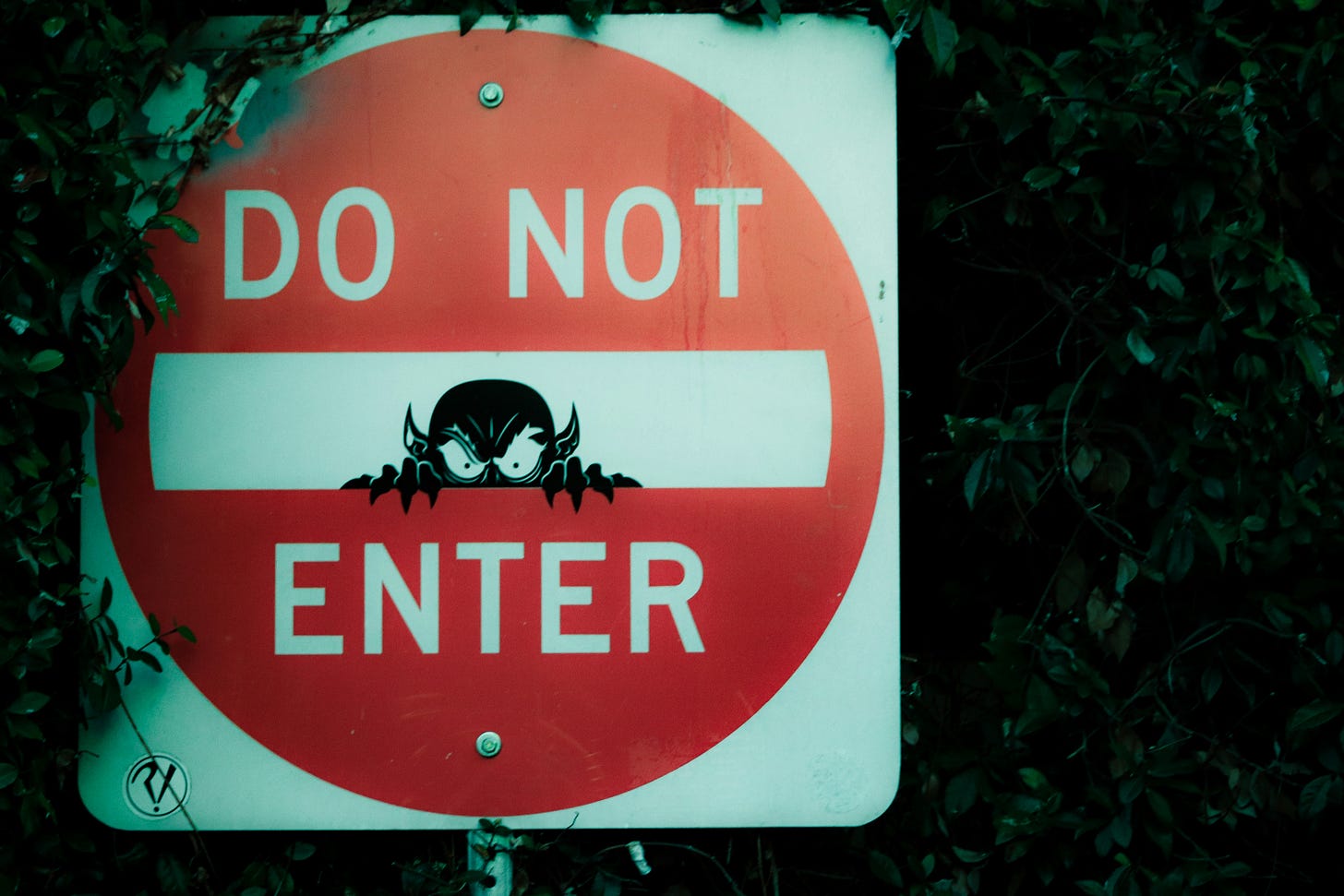 A photo of a red sign that says 'do not enter' with a graffiti image of a devil inside the white bar