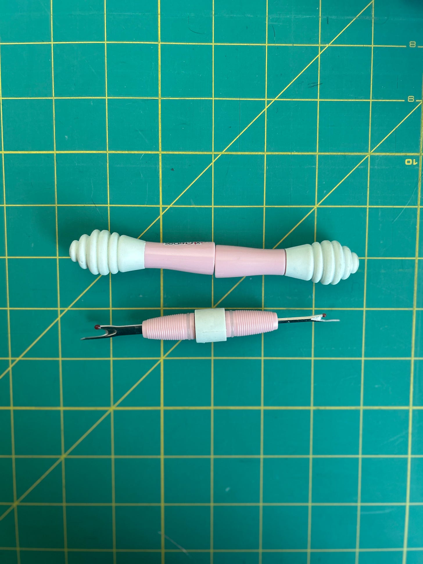 Light pink two sided seam ripper on a green background