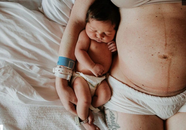 Women after birth with still visible pregnancy bump cuddling a sleepy newborn