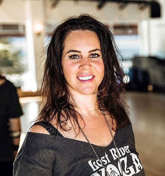 Smiling woman with dark, shoulder-length hair looking straight at you with off the shoulder dark grey Lost River Yoga shirt. Background blurred. Smiling woman with dark, shoulder-length hair looking straight at you with off the shoulder dark grey Lost River Yoga shirt. Background blurred.