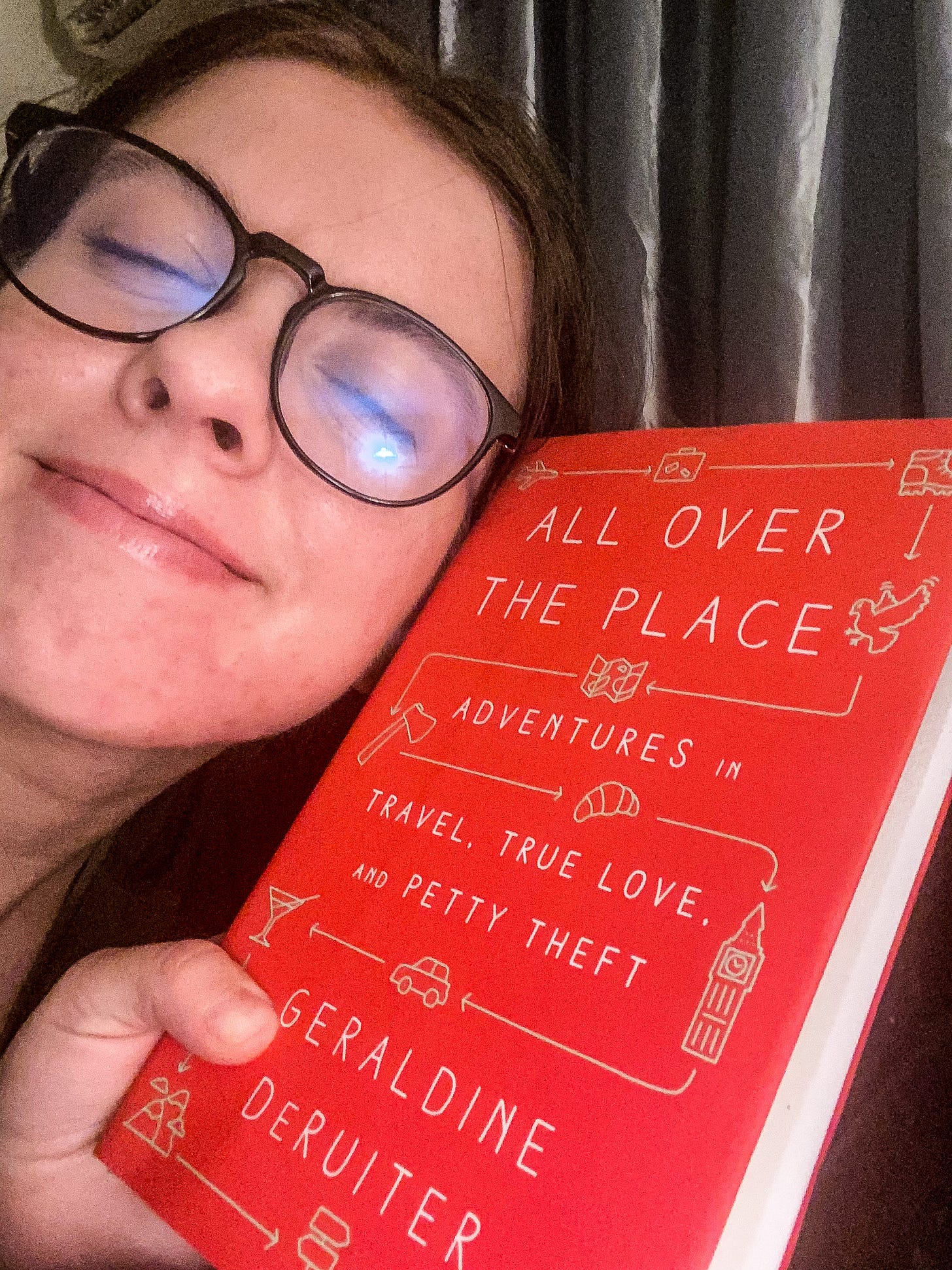 A photo of me smiling like a dork in my blue light glasses while hugging "All Over the Place" - a red book by Geraldine DeRuiter A photo of me smiling like a dork in my blue light glasses while hugging "All Over the Place" - a red book by Geraldine DeRuiter