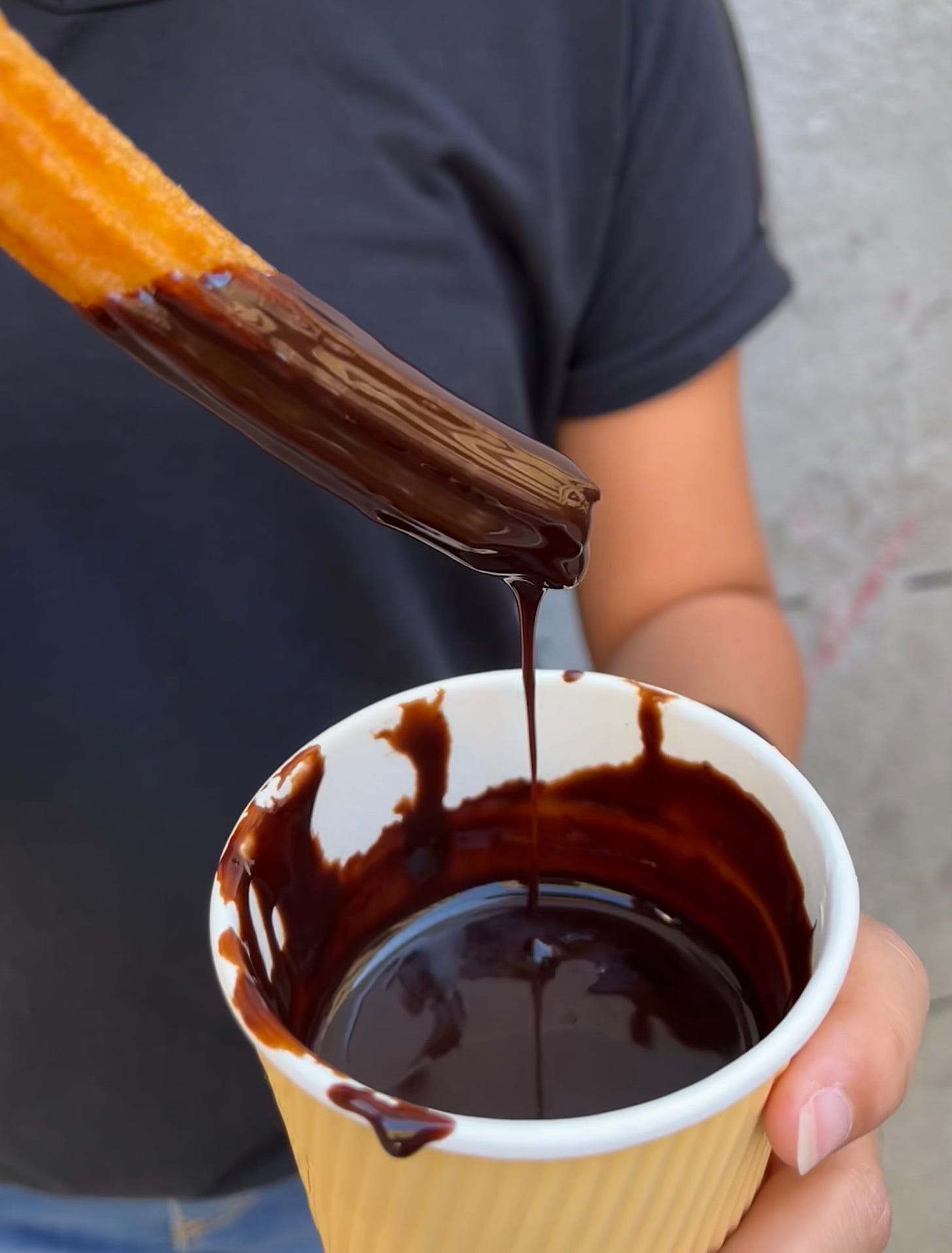 churro dipped into paper cup full of melted chocolate, with chocolate dripping off churro and back into the cup