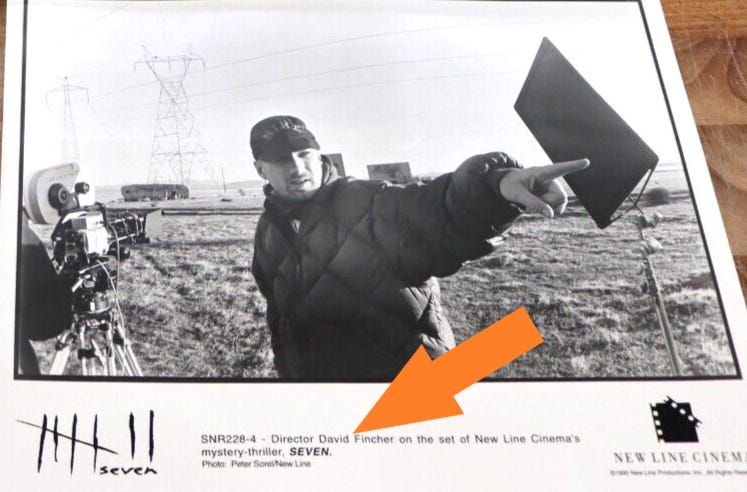 A black-and-white photo from the press kit showing Fincher pointing offscreen. The caption indicates the title is 'Seven.'