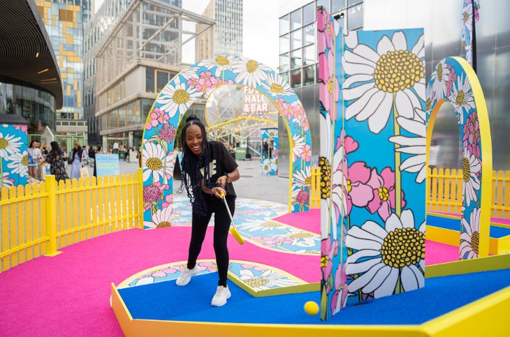 A woman playing mini golf on a yellow, pink and blue pop-up golf course