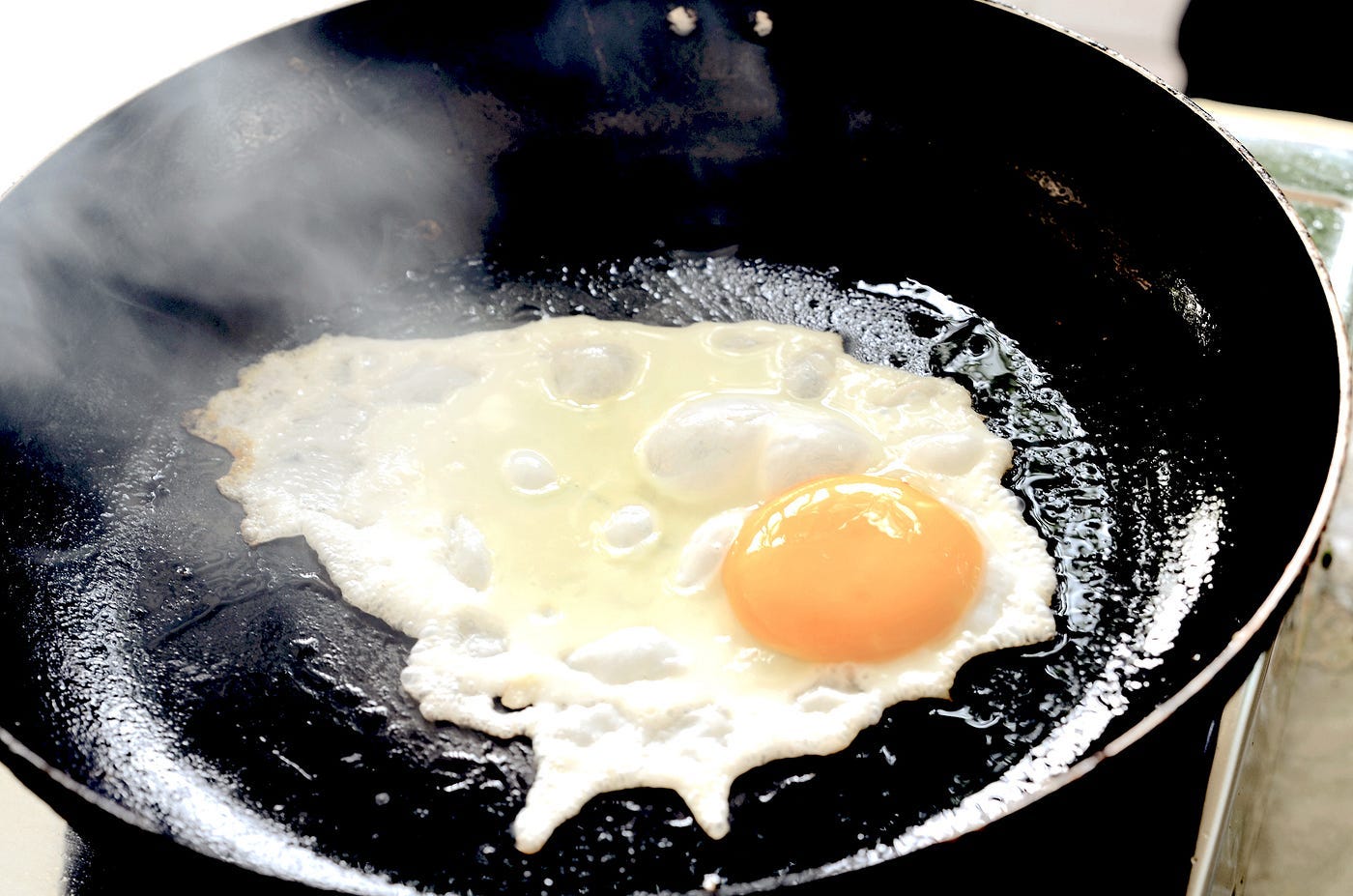 Egg frying in pan with smoke emerging.
