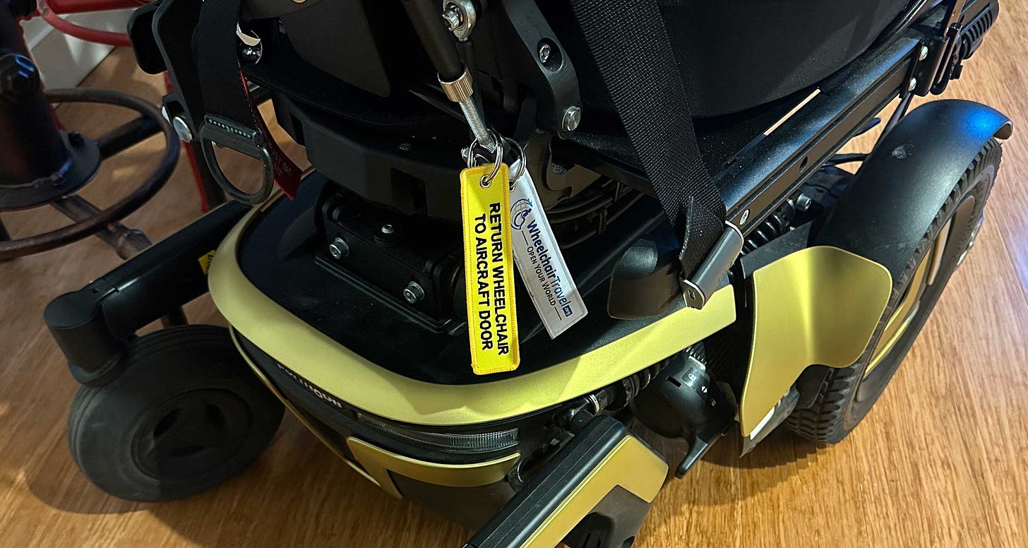 Yellow luggage tag attached to a power wheelchair with embroidered black text that reads, Return Wheelchair to Aircraft Door.