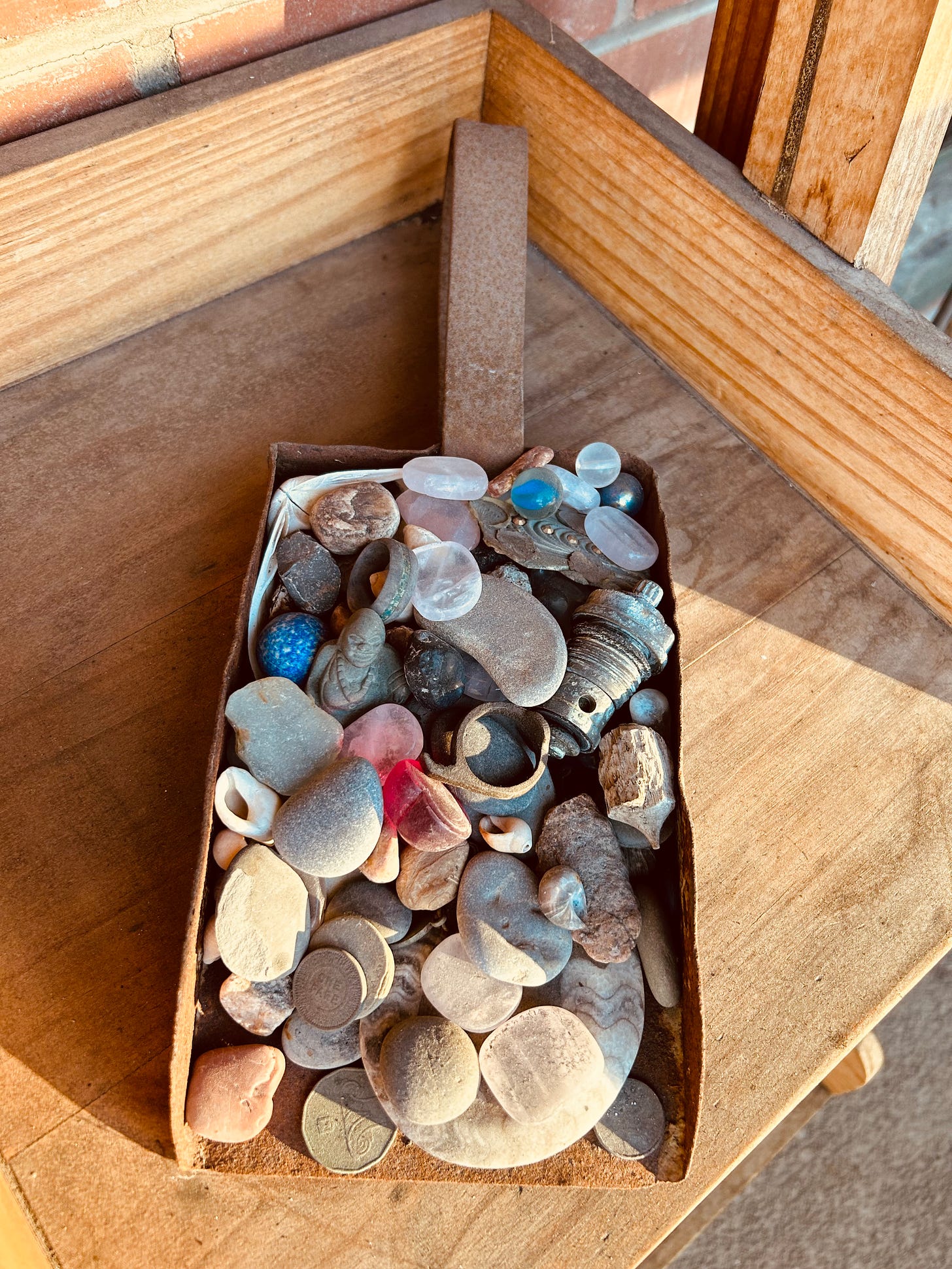 A shovel full of found objects: stones, bubble glass, rings, broach.