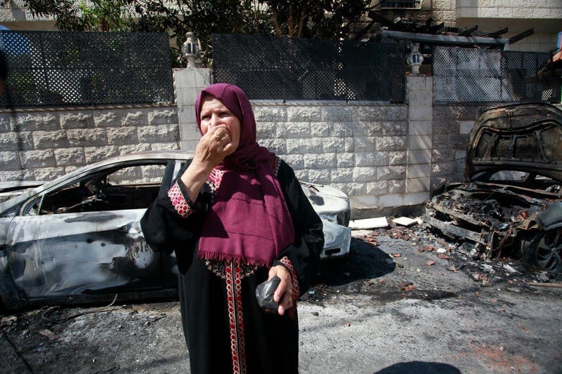 A woman stands in the street near burned vehicles 