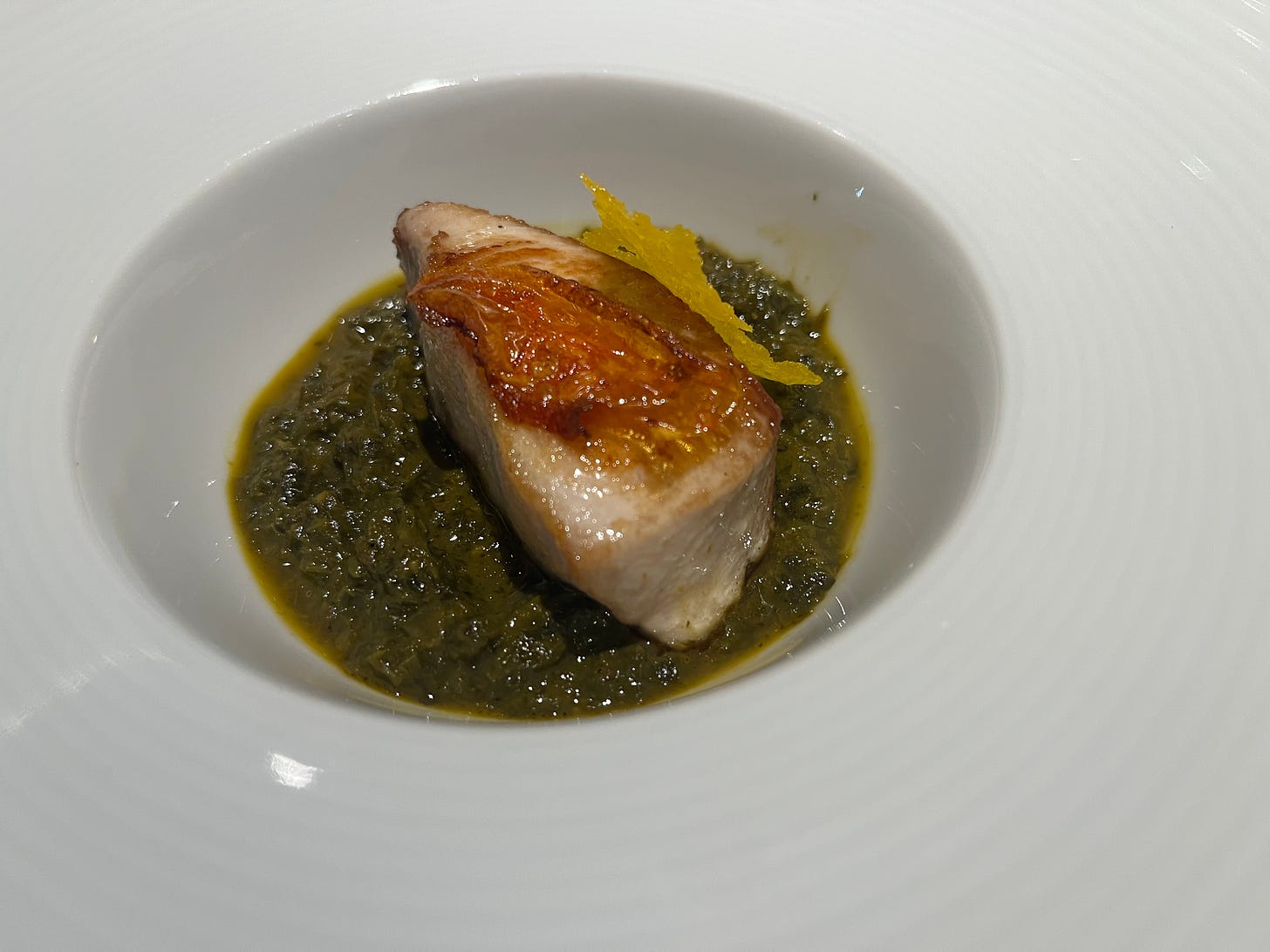A piece of grilled fish on a green sauce, with a yellow chip on top
