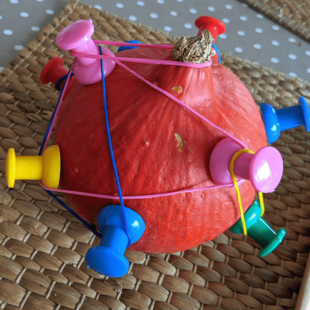 a pumpkin and giant drawing pins have been used to create a geoboard