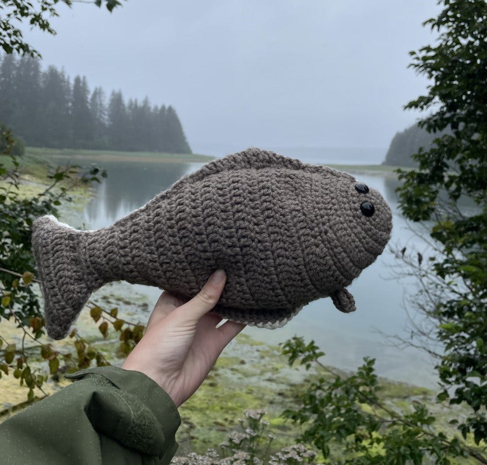 A crocheted halibut fish being held up by a hand.