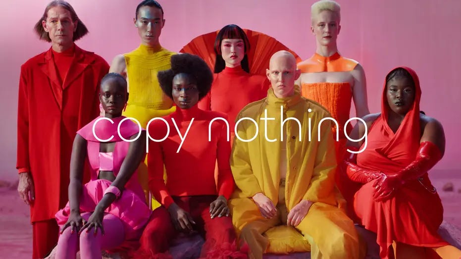 A diverse group of individuals dressed in bold, vibrant colors, sitting and standing against a pink backdrop. The words "copy nothing" are prominently displayed in the center, reflecting the theme of individuality and uniqueness.