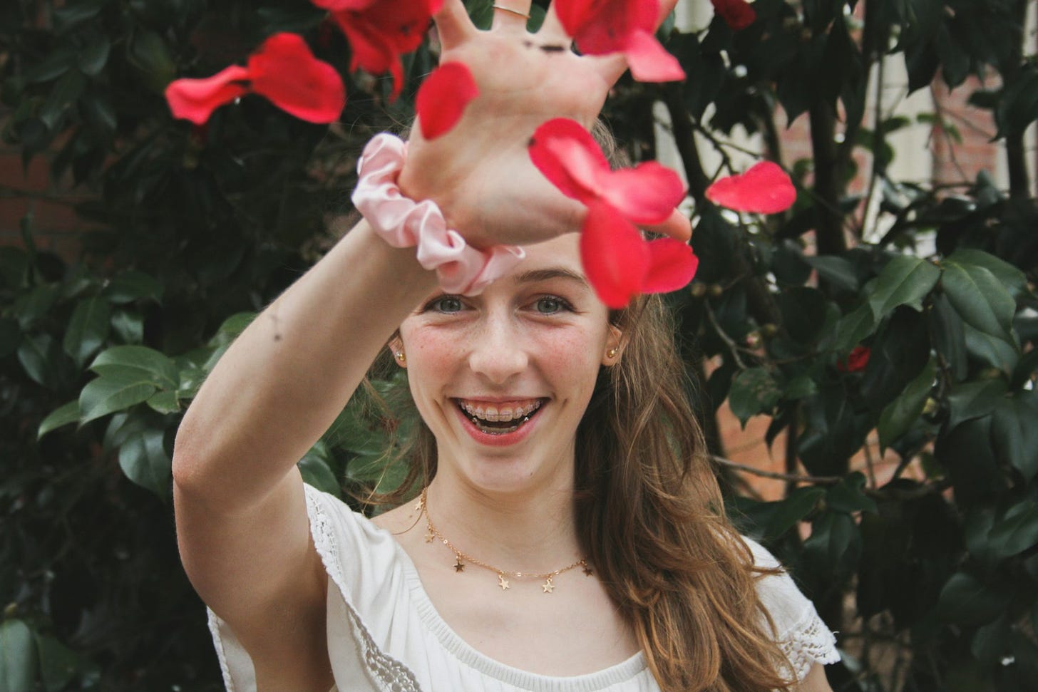 Young woman with brown hair in white top throwing petals into the air.