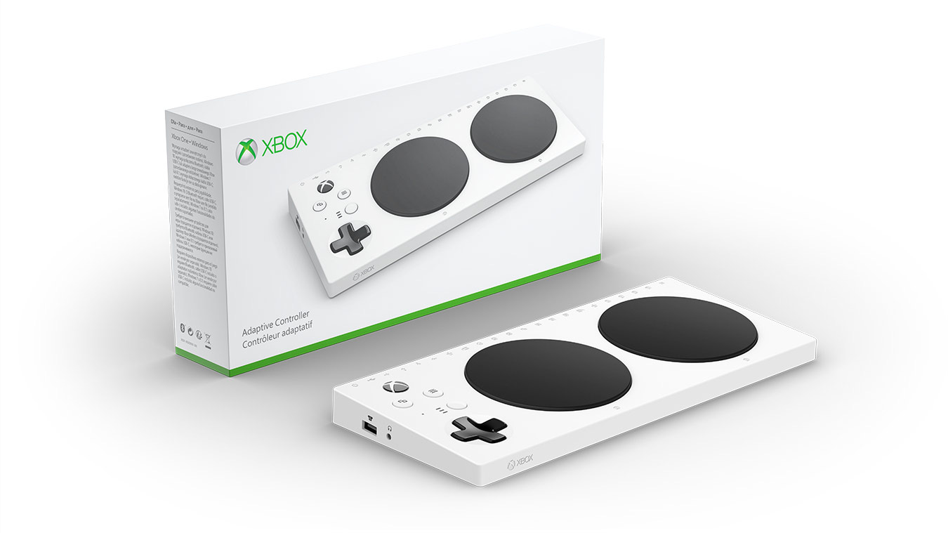 A white Xbox Adaptive Controller with a black pad, sitting on top of its open box. The controller is positioned in the center of the image, while the box is located to its right.