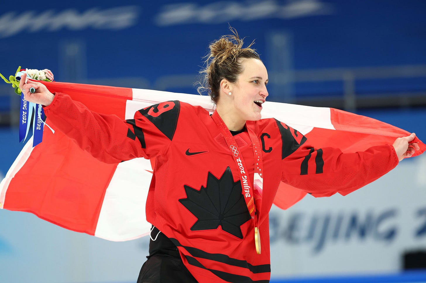 Marie-Philip Poulin holds the Canadian flag behind her as she celebrates winning a gold medal at the Olympics.