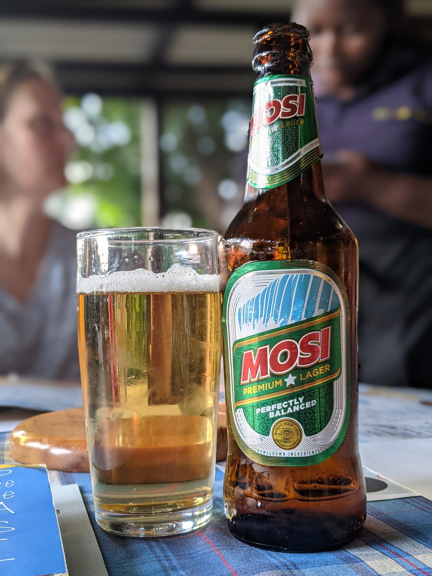 Photo of a bottle of beer called Mosi, featuring a picture of a waterfall on the label. A glass of beer sits next to the open bottle.