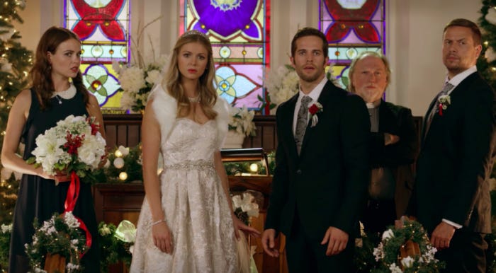 Movie still from Christmas Wedding Planner. A couple stand at an altar with their wedding party, looking disgusted and decked out in Christmas decorations.