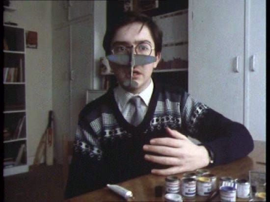 Adrian Mole from the 1980s TV show sitting with a model plane glued to his nose