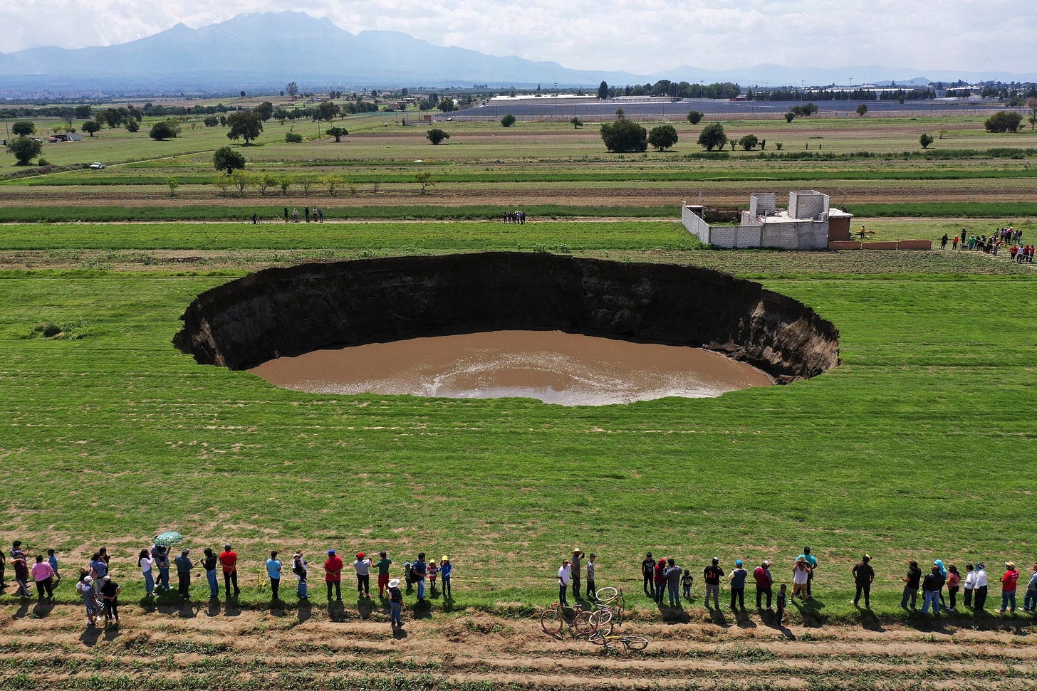 Aerial view of people standing around a sinkhole that was found by farmers in a field of crops in Santa Maria Zacatepec...