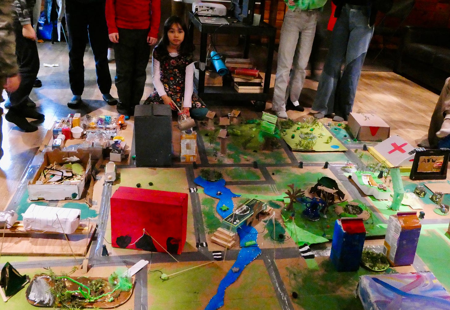 girl sitting next to large diorama made from recycled materials
