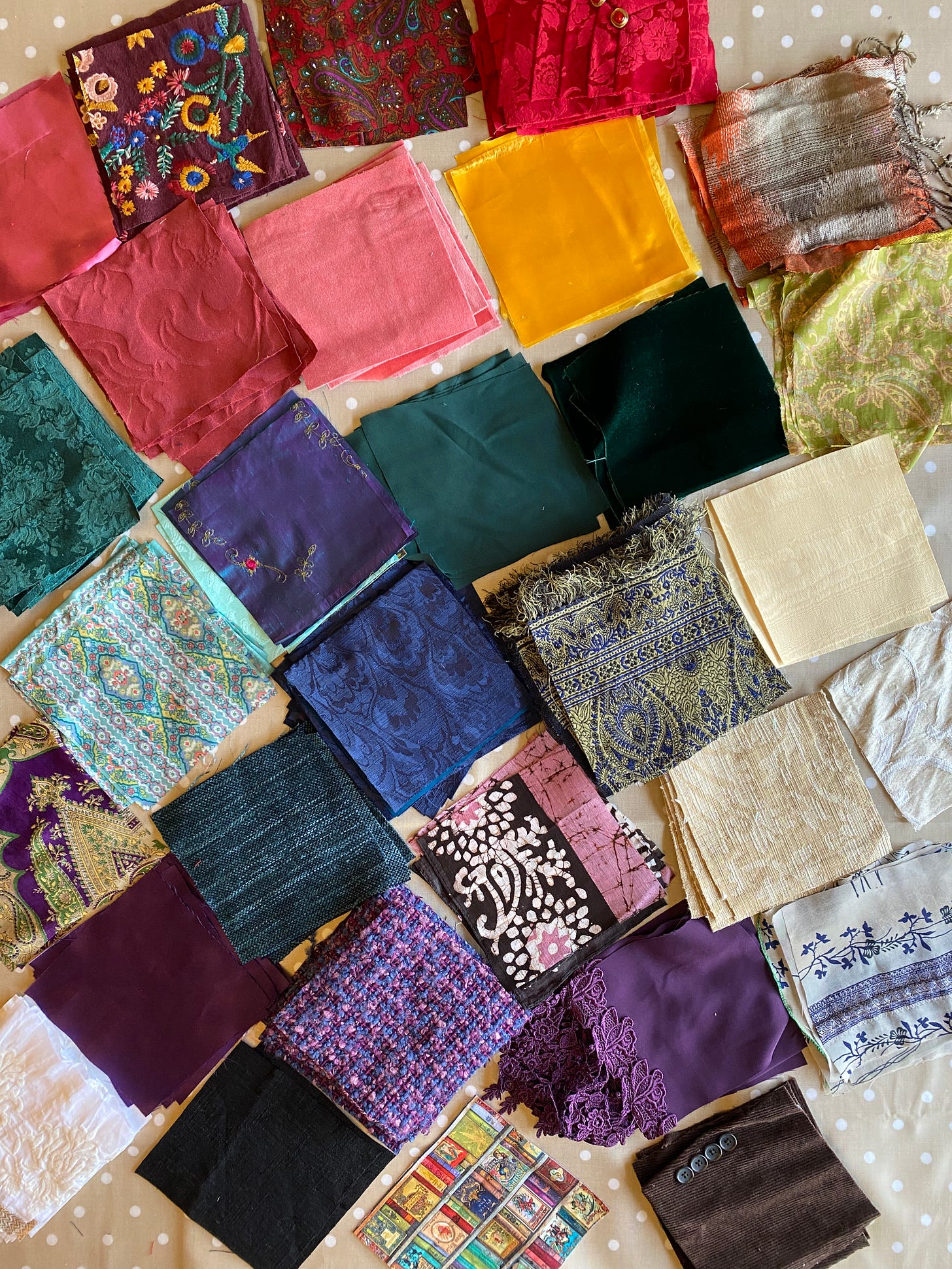 Piles of 209 square patches sorted by colors: red, gold, yellow, blue, green, purple, white, brown, black. There are also various textures: velvets, brocade, silk, corduroy, satin, batik, embroidered, and a red pleated satin with a row of red and gold buttons.