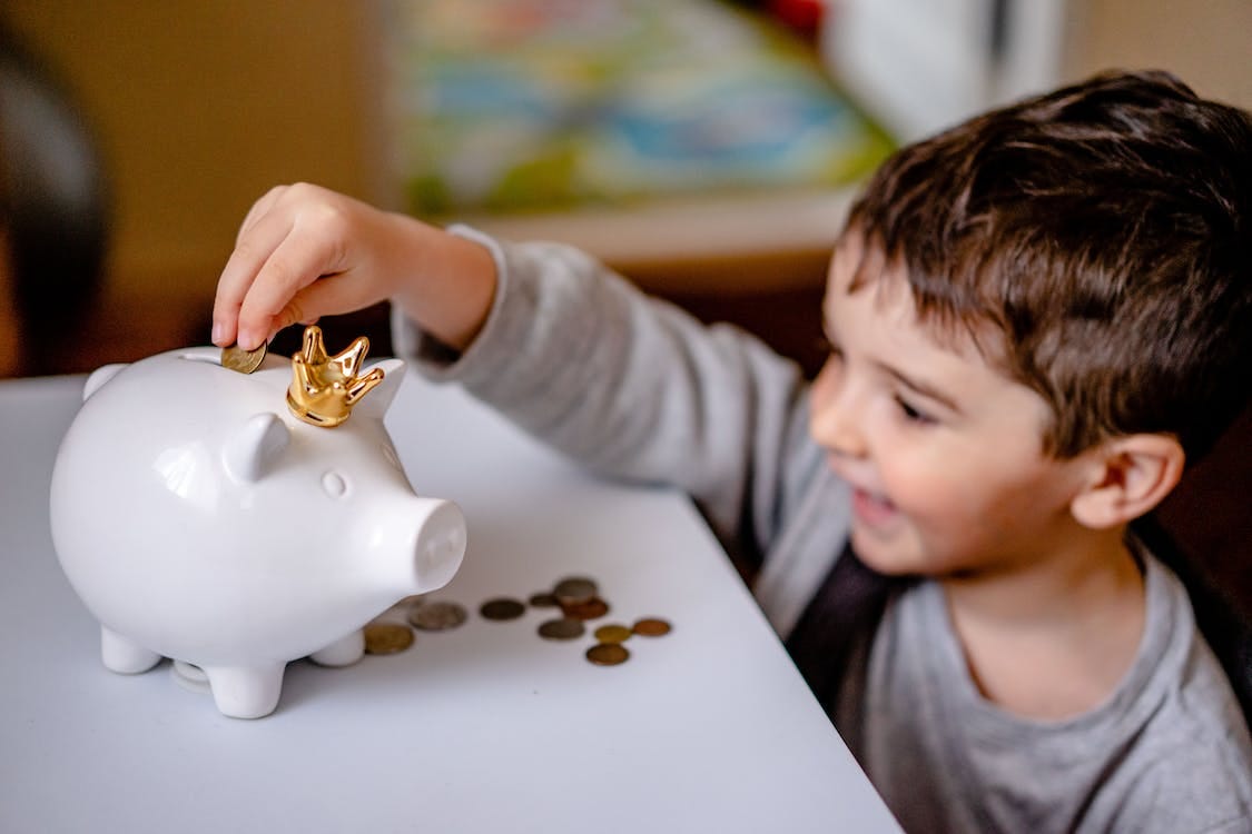 Boy in Gray Long Sleeve Shirt Putting Coins in a Piggy Bank