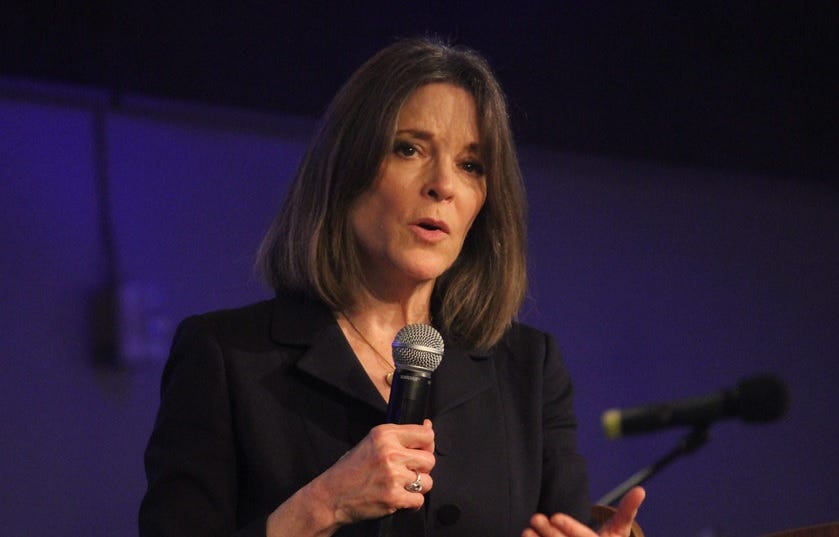 Photo of Marianne Williamson  speaking and holding a mic 