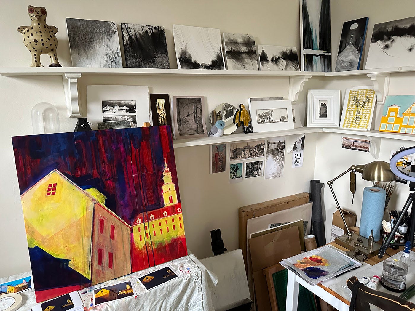 Photo of my studio, with large panel in progress on a table, and shelves holing a lot of black and white art
