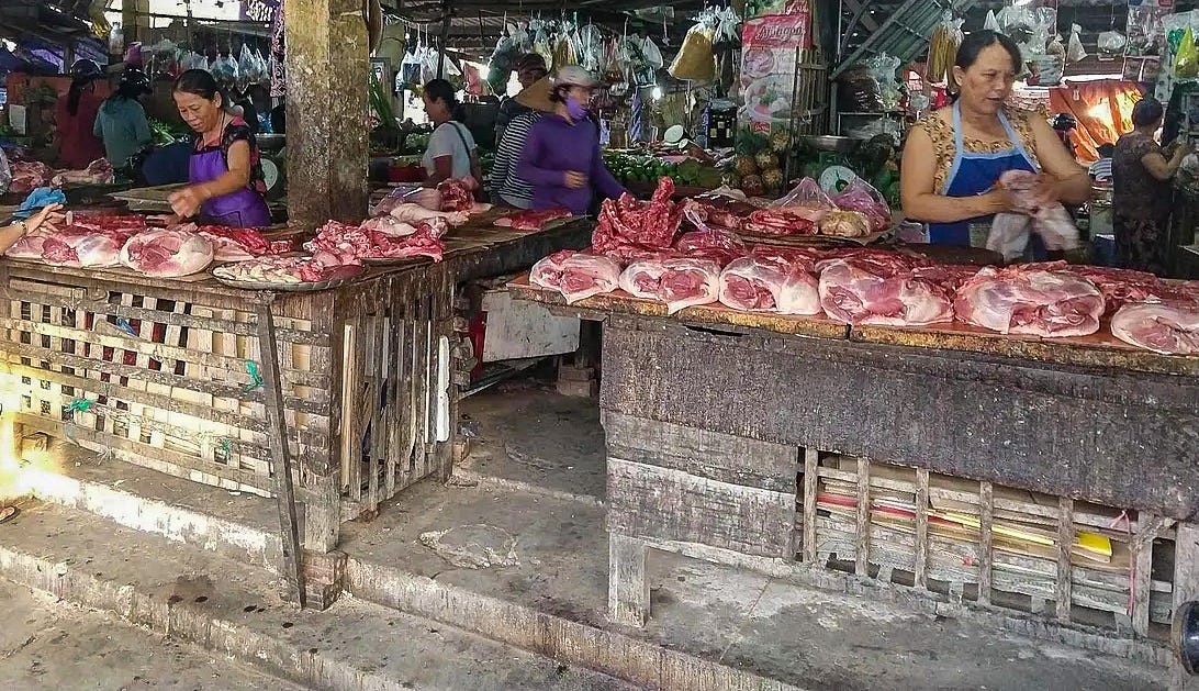 Two women selling large chunks of meat from primitive-looking countertops. 