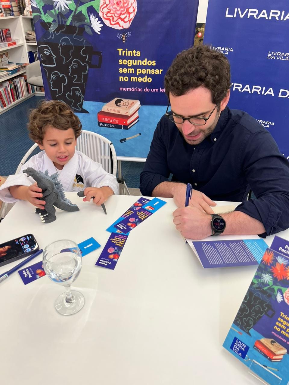 Pedro Pacífico autografa o livro enquanto Arthur brinca com um boneco do Godzilla 