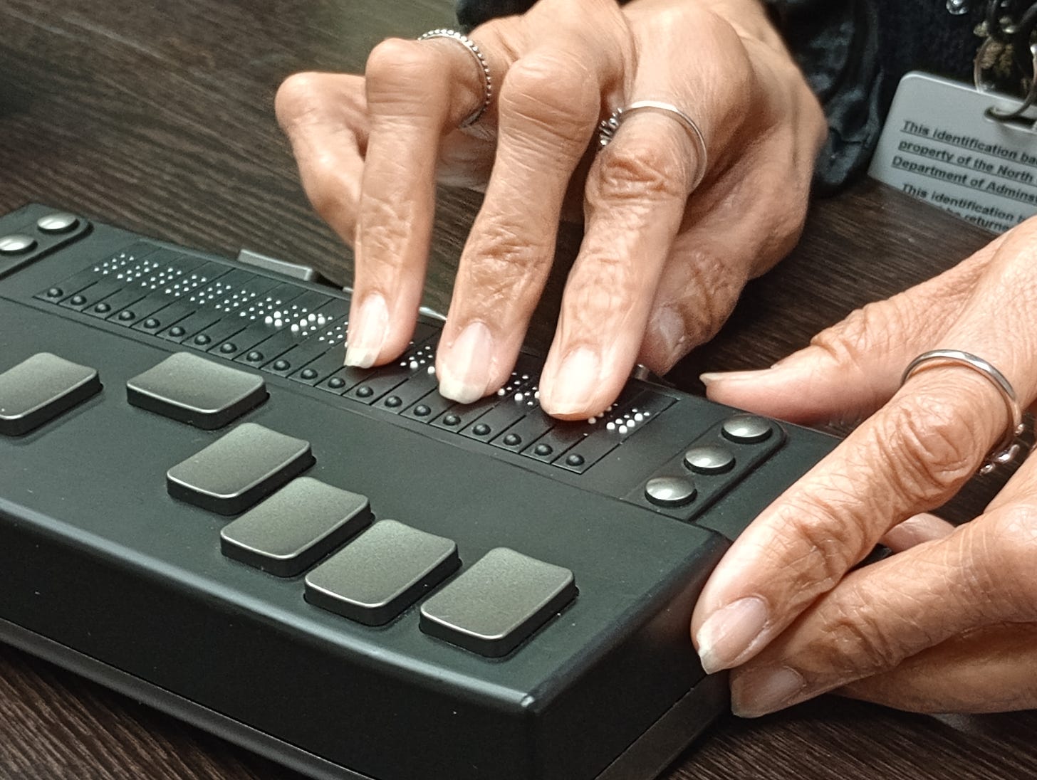 A closeup of a person's hands using a Braille eReader, a small portable electronic reading device for braille users.