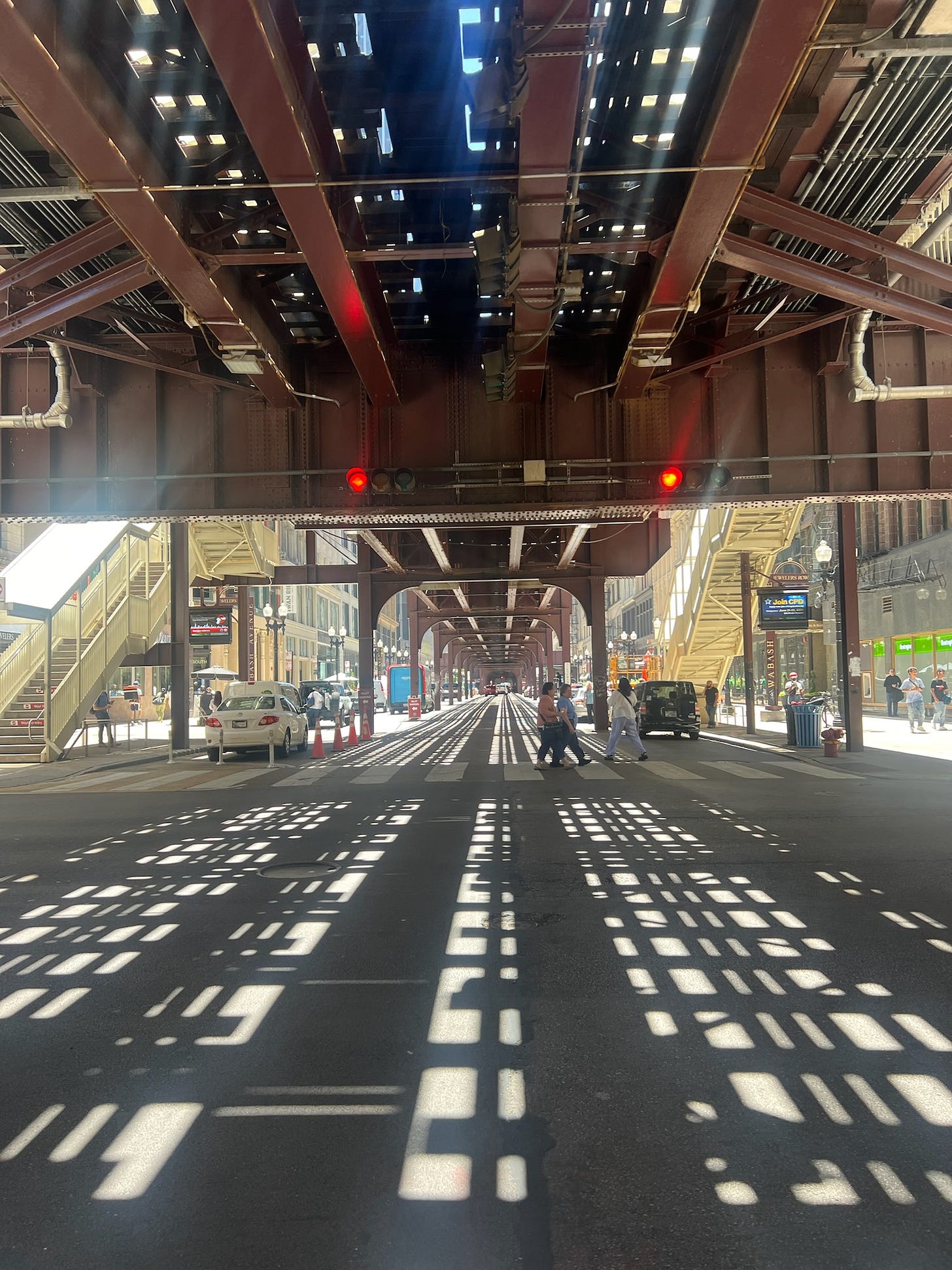 People walking beneath an elevated train on a sunny day.