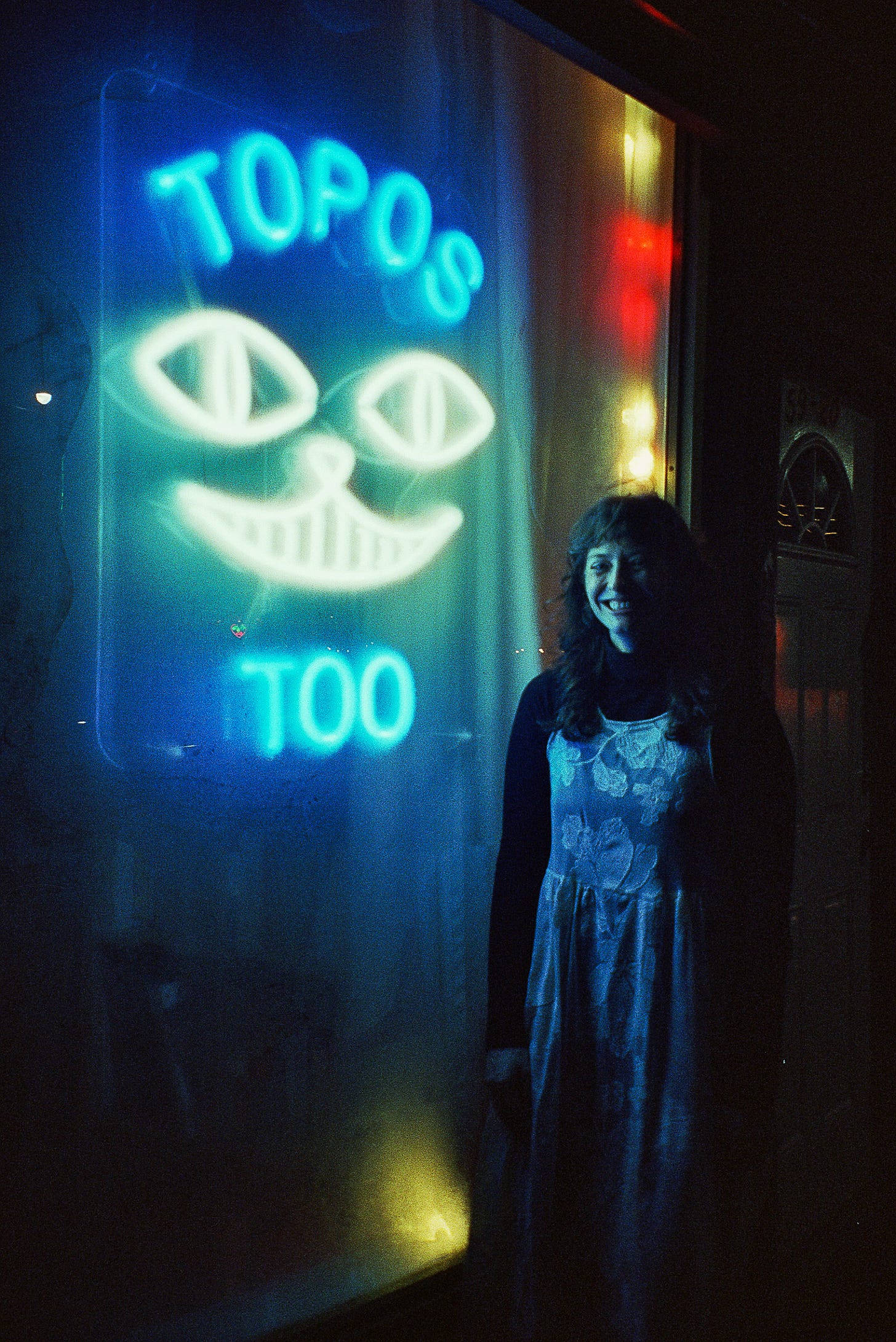 Marissa smiling outside the neon sign for Topos Too