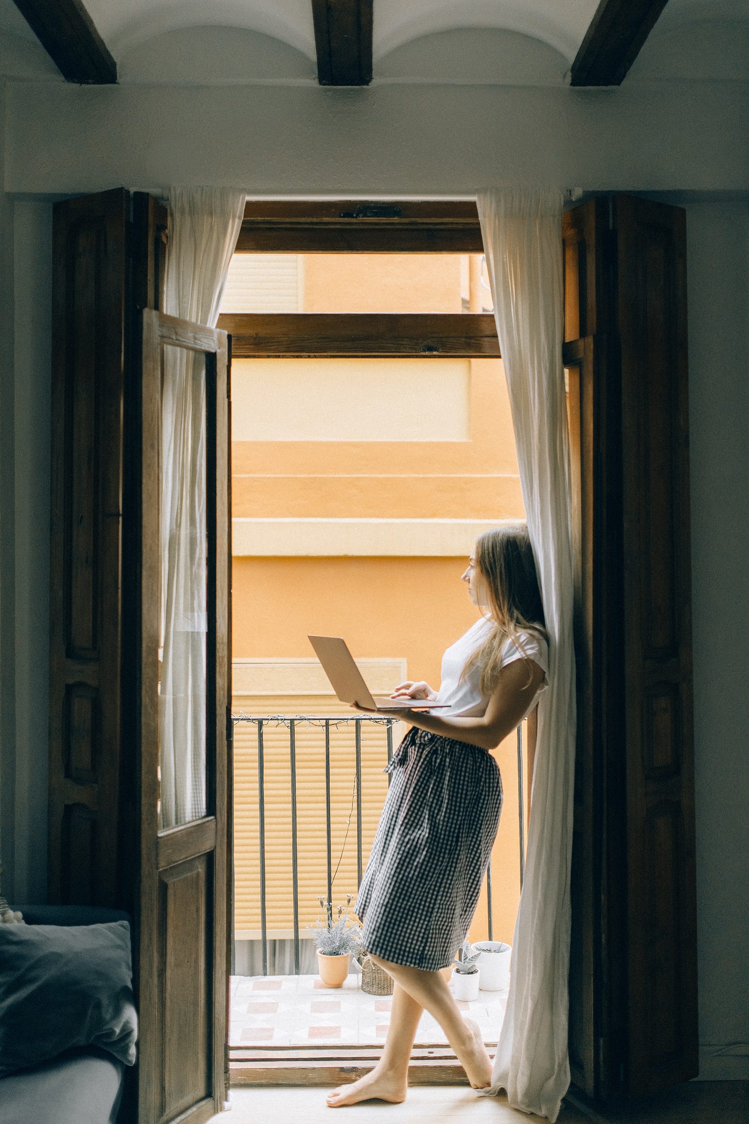 Young woman holding laptop looking out of open door.