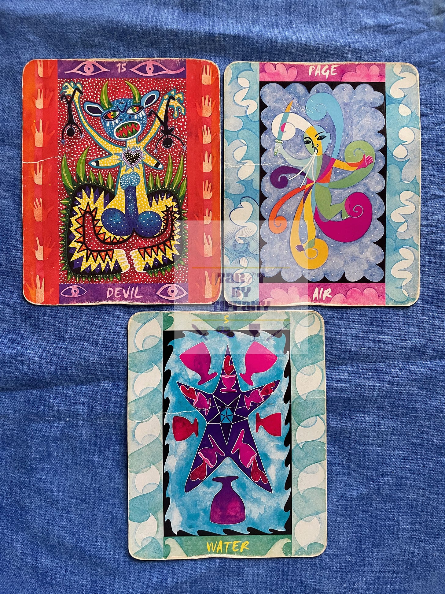 3-card reading with the Tarot of the Four Elements. The cards are laid against a cobalt blue cloth background. Top two cards (L-R): 15 - Devil, Page of Air. Bottom card: 5 of Water.