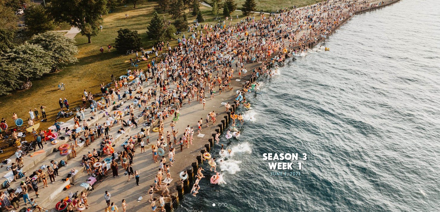 aerial photo of hundreds of people with colorful swim floaties on the banks of Lake Michigan about to swim